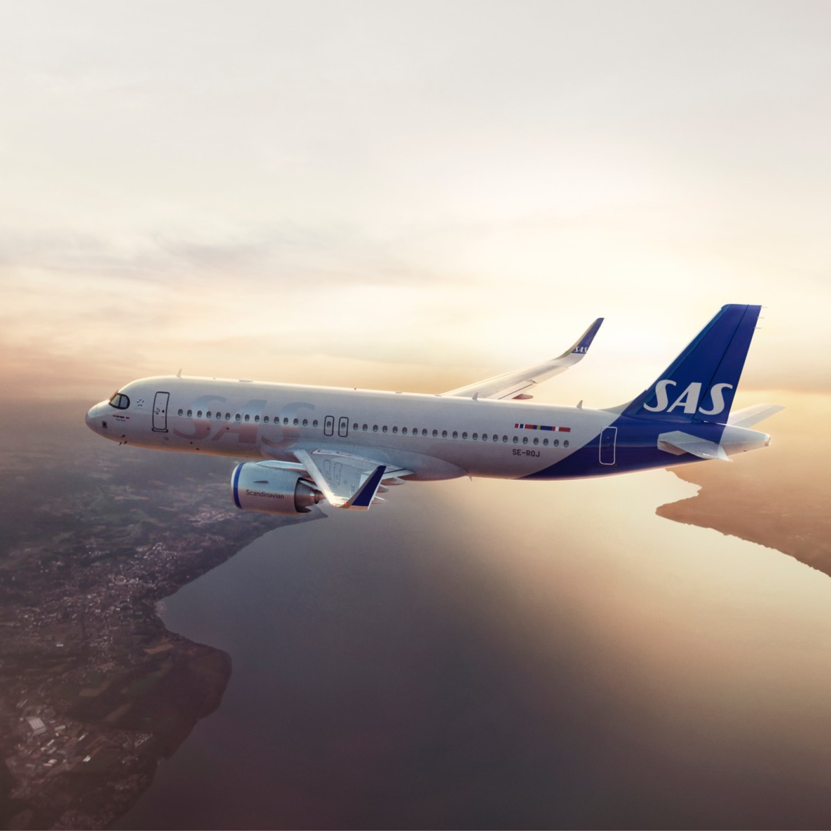 AbraCasaBra.se Ett passagerarflygplan från SAS flyger över ett vattendrag i solnedgången, med land synligt nedanför och en molnig himmel i bakgrunden.